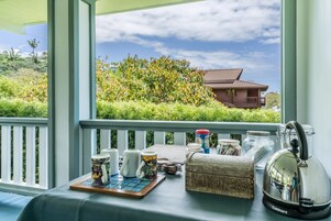 A table with kitchenware and a kettle on a balcony with a view of a house and greenery.