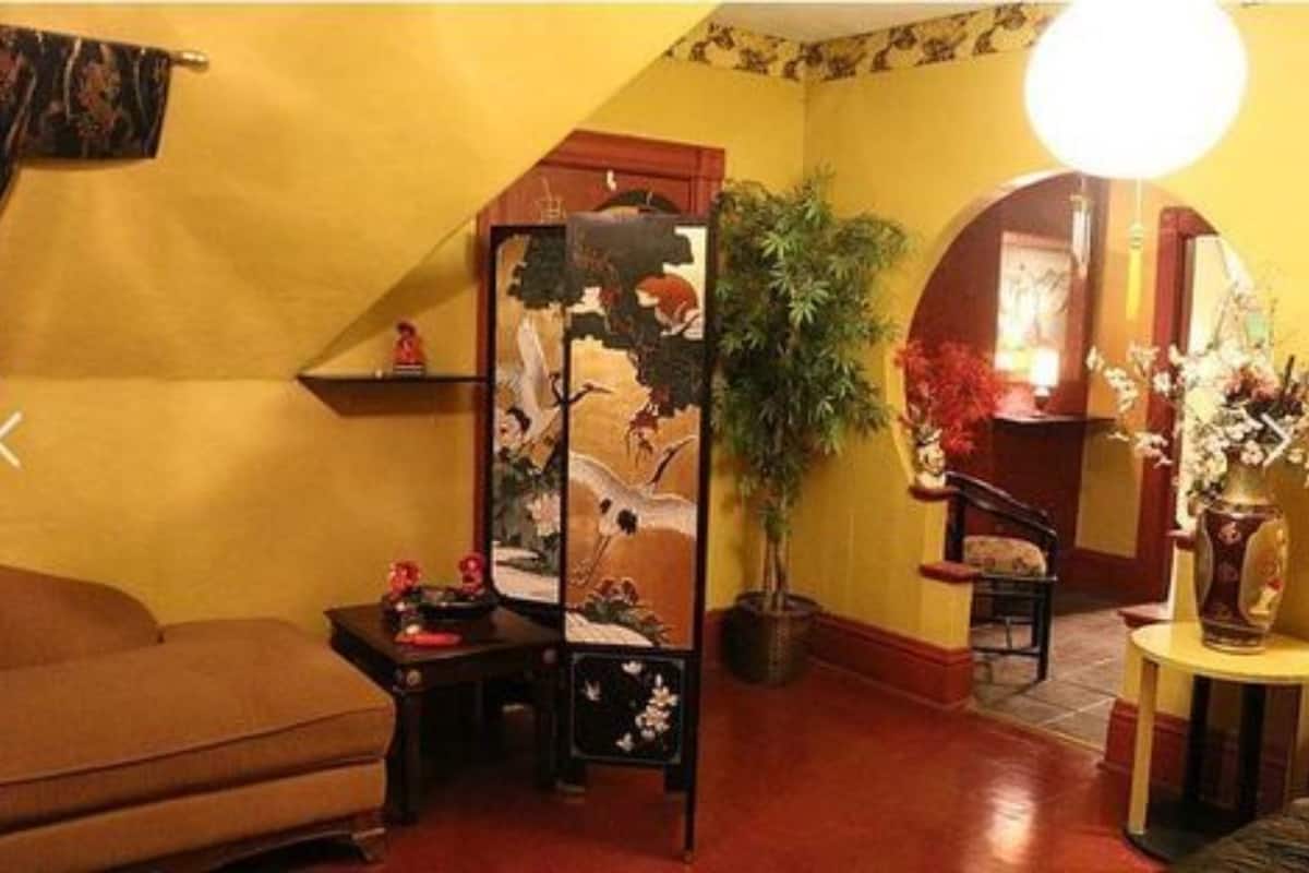 Quarto tradicional com sofá, um biombo decorativo, planta em vaso e uma mesinha com um vaso.