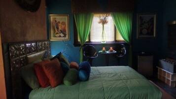 Un dormitorio con cama, cortinas verdes, una mesita con velas y un florero con flores.