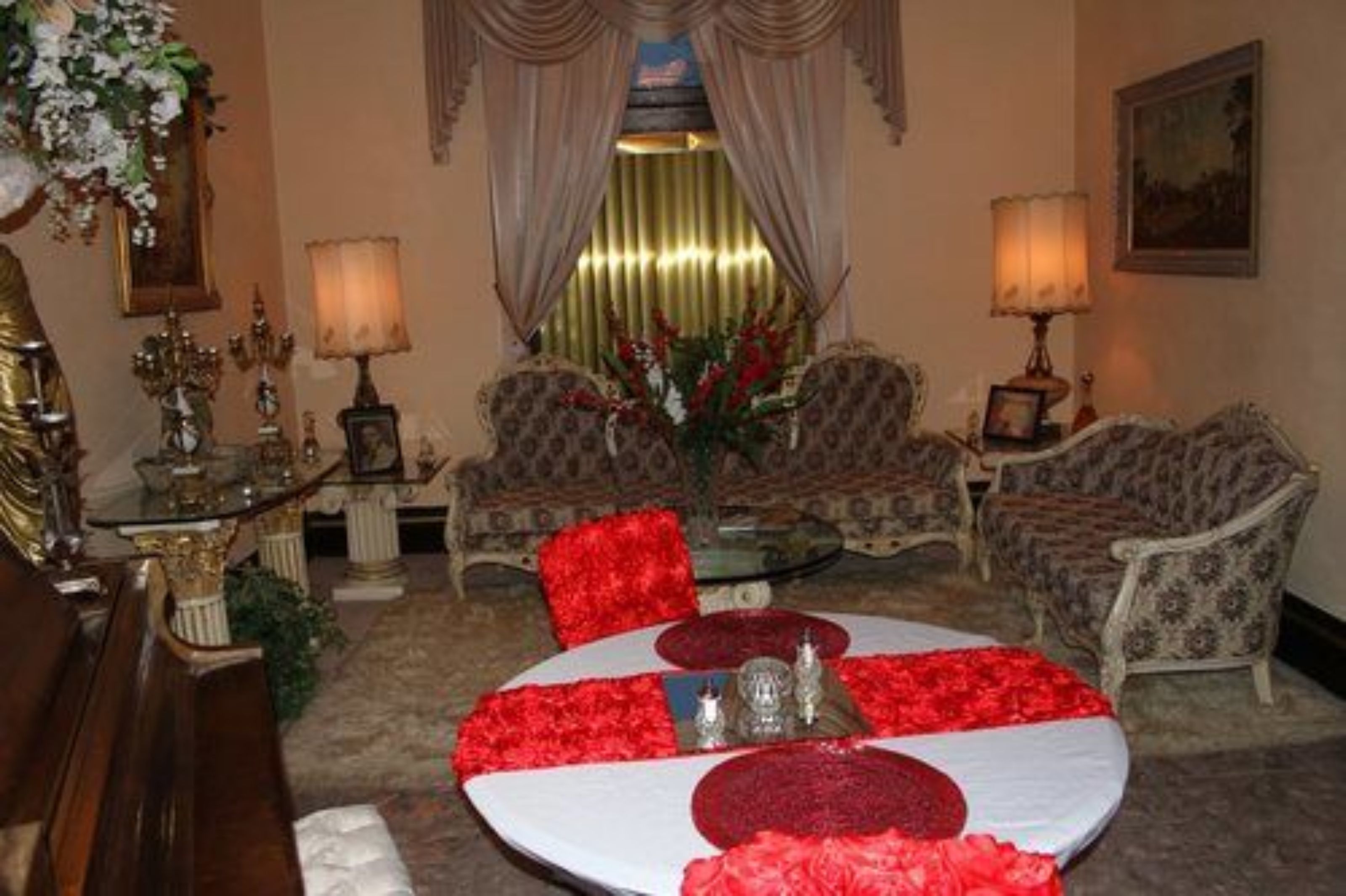 Un salón formal con una mesa redonda dispuesta para comer, rodeado de sillones con reposabrazos y un sofá estampado.