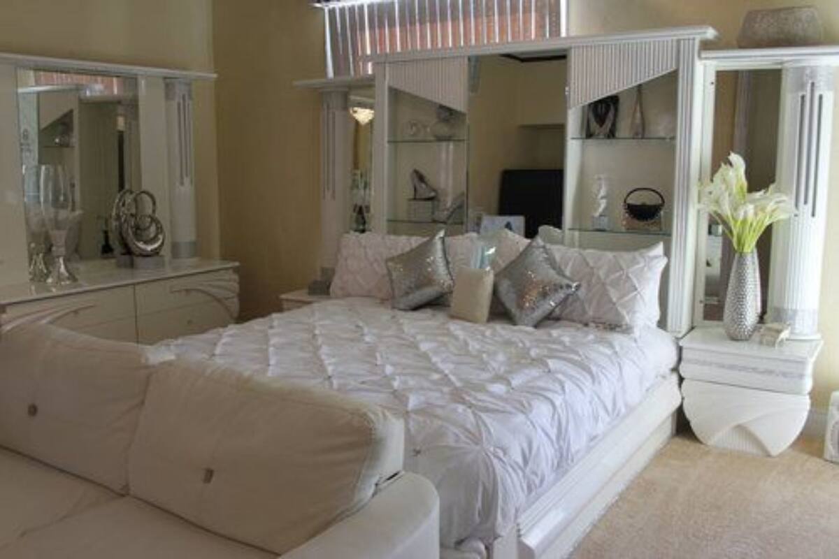 Quarto com uma cama grande, penteadeira, espelho e mesa de cabeceira com um vaso.