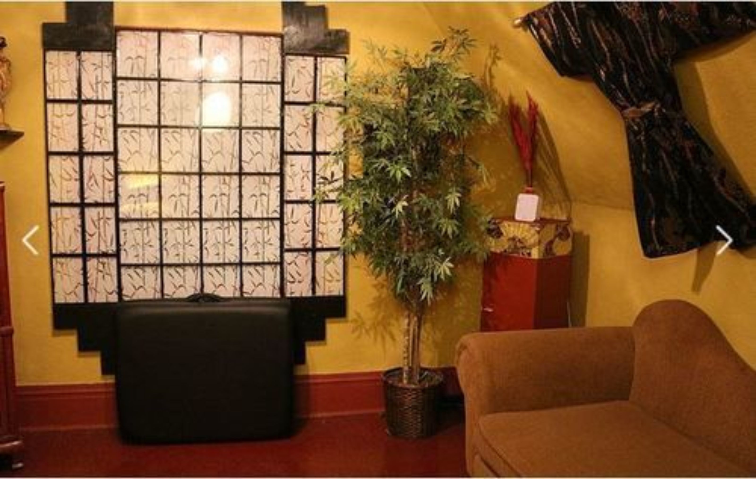 A room with a large wall-mounted artwork, a potted plant, a sofa, and a small table with a decorative item.