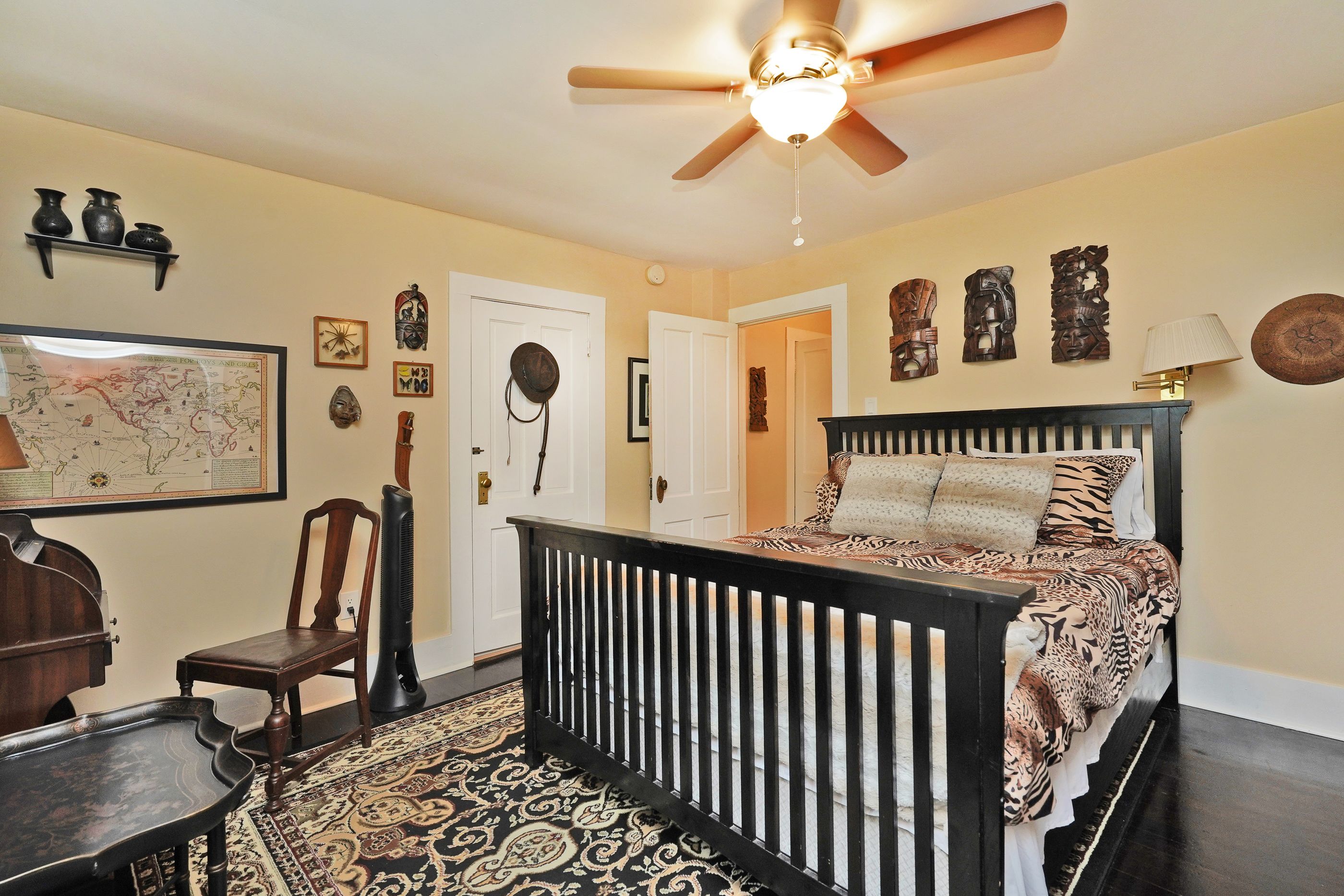 A bedroom with a bed, a ceiling fan, a map on the wall, and a wooden dresser.