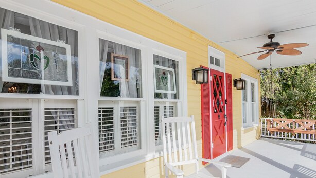 A yellow building with white-framed windows, a red door, and a white porch with chairs. - The Wayward Traveler's Inn (Mims)