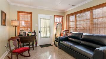 A living room with a black leather sofa, a wooden rocking chair, a dining table with chairs, and a large mirror.