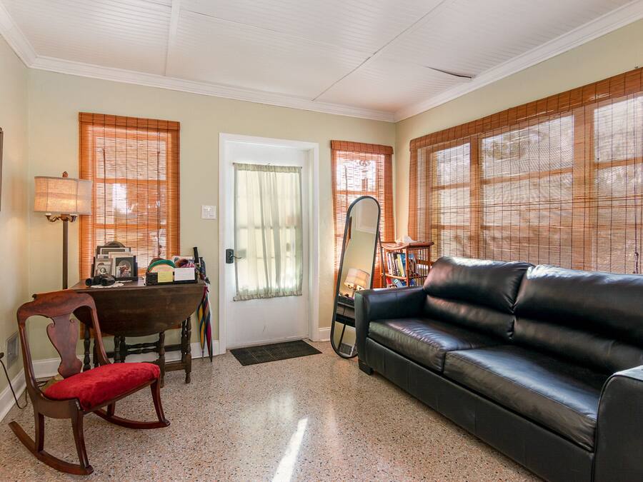 A living room with a black leather sofa, a wooden rocking chair, a dining table with chairs, and a large mirror.