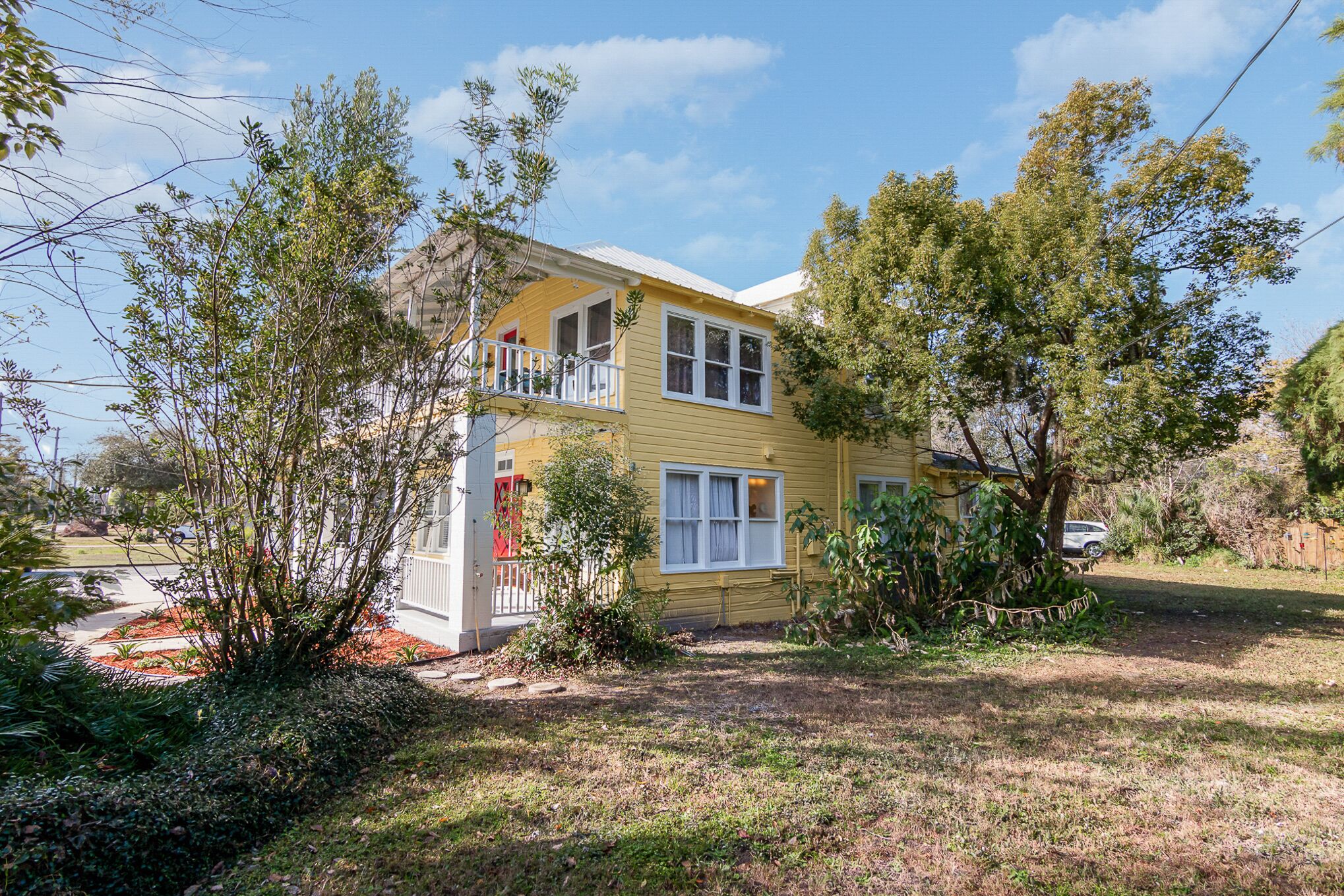 A two-story yellow house with a balcony, surrounded by trees and a well-maintained lawn.