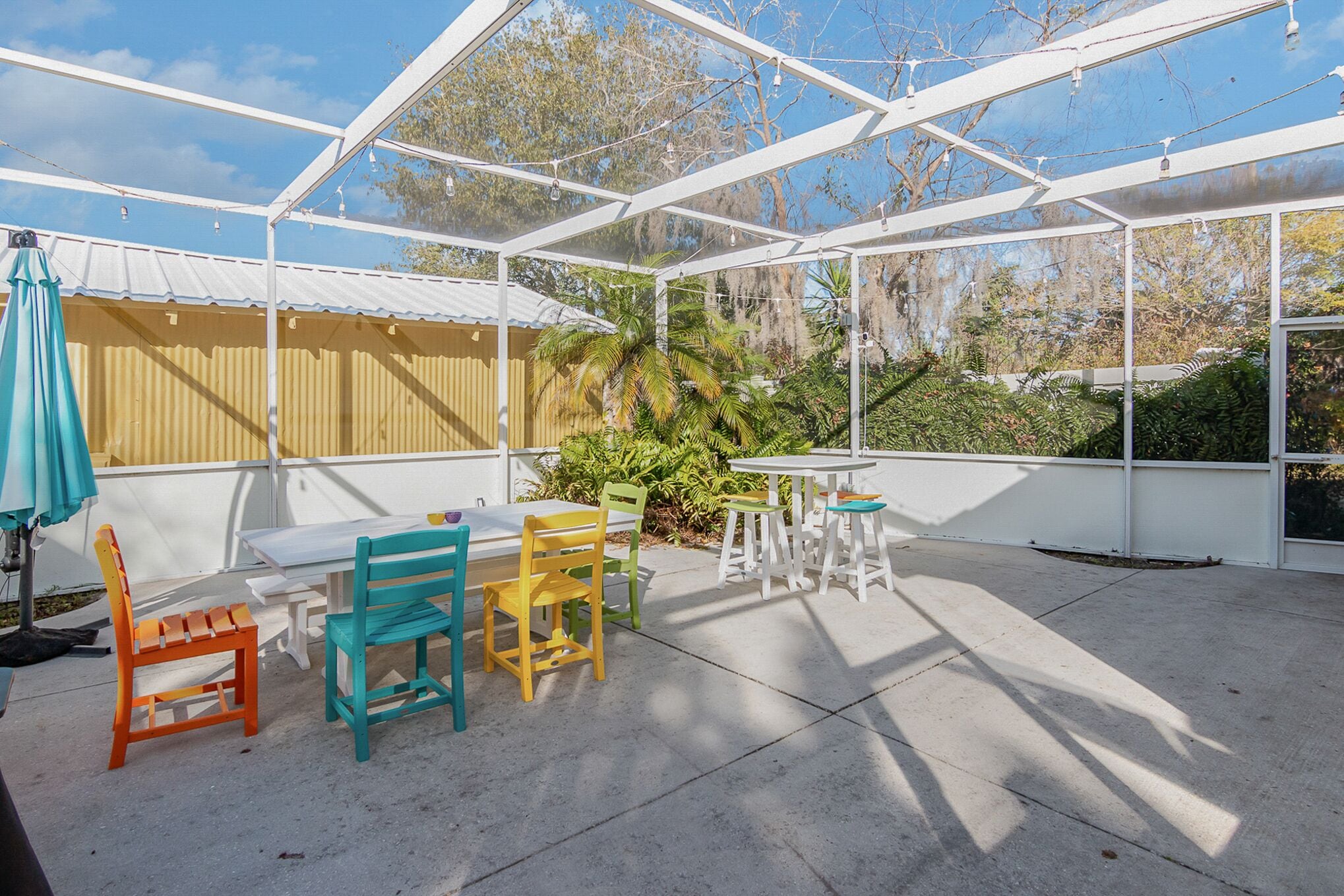 Uma área de varanda coberta com mesa, cadeiras, um banco e um guarda-sol suspenso.
