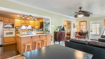 A kitchen with wooden cabinets, a microwave, and a breakfast bar with stools. There is a ceiling fan and a dining area with a table and chairs.