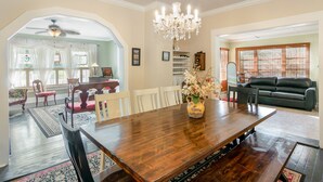 A dining area with a wooden table, chairs, a chandelier, and a vase with flowers. - The Wayward Traveler's Inn (Mims)
