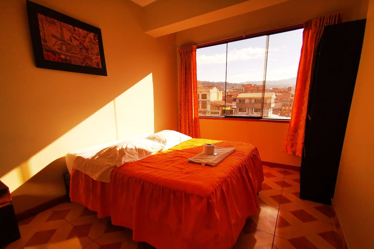 Quarto com cama, janela com cortinas, quadro na parede e piso ladrilhado.