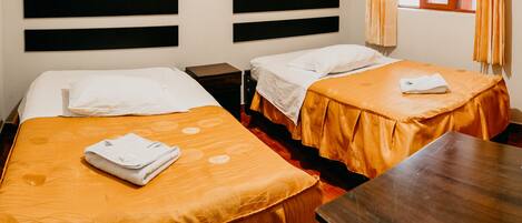 A hotel room with two beds, each with a white pillow and a folded towel on the bed. There is a wooden nightstand between the beds and a wooden table in the room.