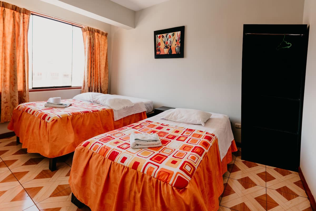 Quarto de hotel com duas camas, janela com cortinas, um quadro na parede e um guarda-roupa preto.