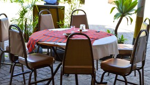An outdoor dining area with a round table covered by a red and black checkered tablecloth, surrounded by wicker chairs. - West Park (Nairobi)