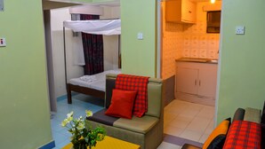 A compact room with a bunk bed, a small sofa with a red blanket, and a kitchenette in the background. - West Park (Nairobi)