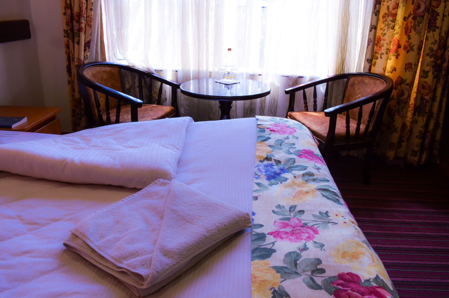 A hotel room with a bed, two chairs, a small table, and a window with curtains.