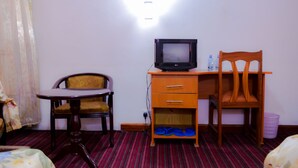 Habitación de hotel con escritorio de madera, televisor, silla, cama y alfombra a rayas.