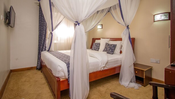 Camera d'albergo con letto a baldacchino, un comodino in legno, un tavolino e una TV a parete.