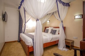 A hotel room with a four-poster bed, a wooden nightstand, a bedside table, and a wall-mounted TV. - Wida Resort Kilimani (Nairobi)