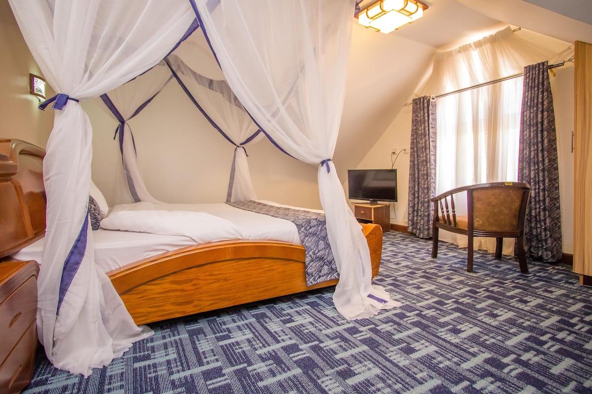 A room with a wooden bed, a chair, a desk, and a television.