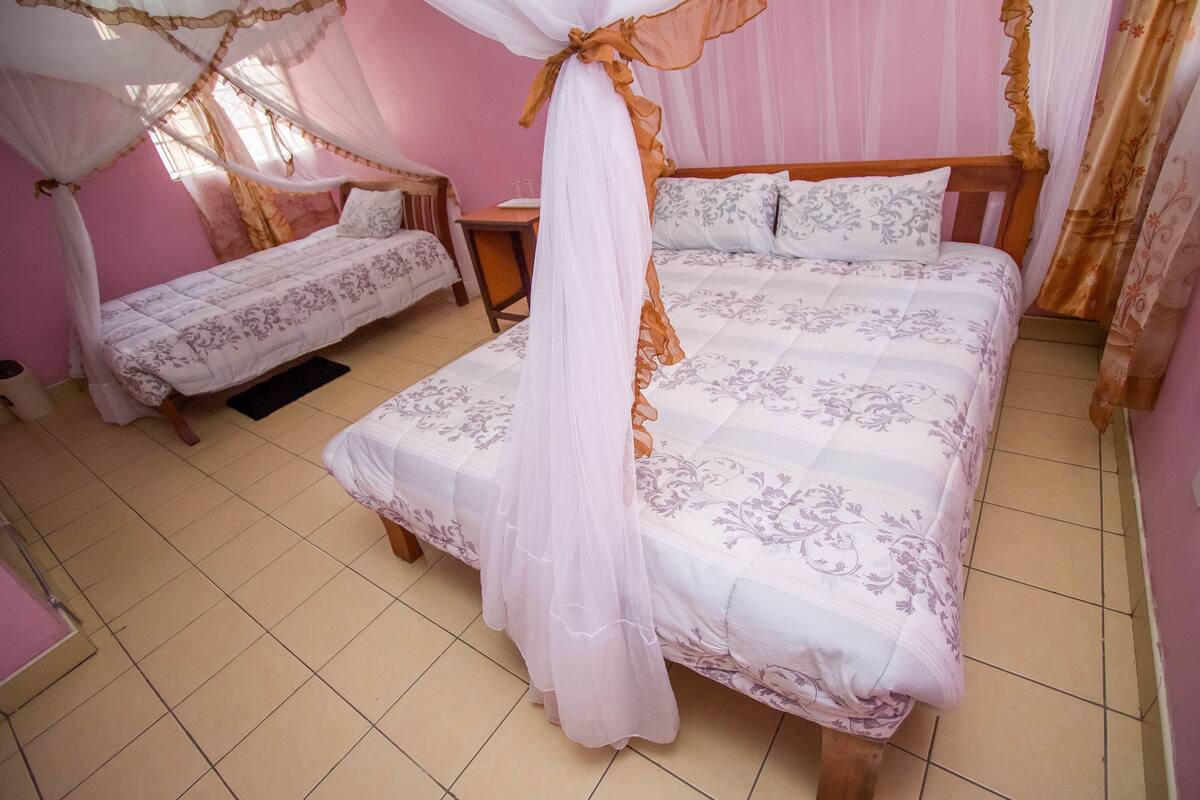 A bedroom with two beds, a mosquito net, and a tiled floor.