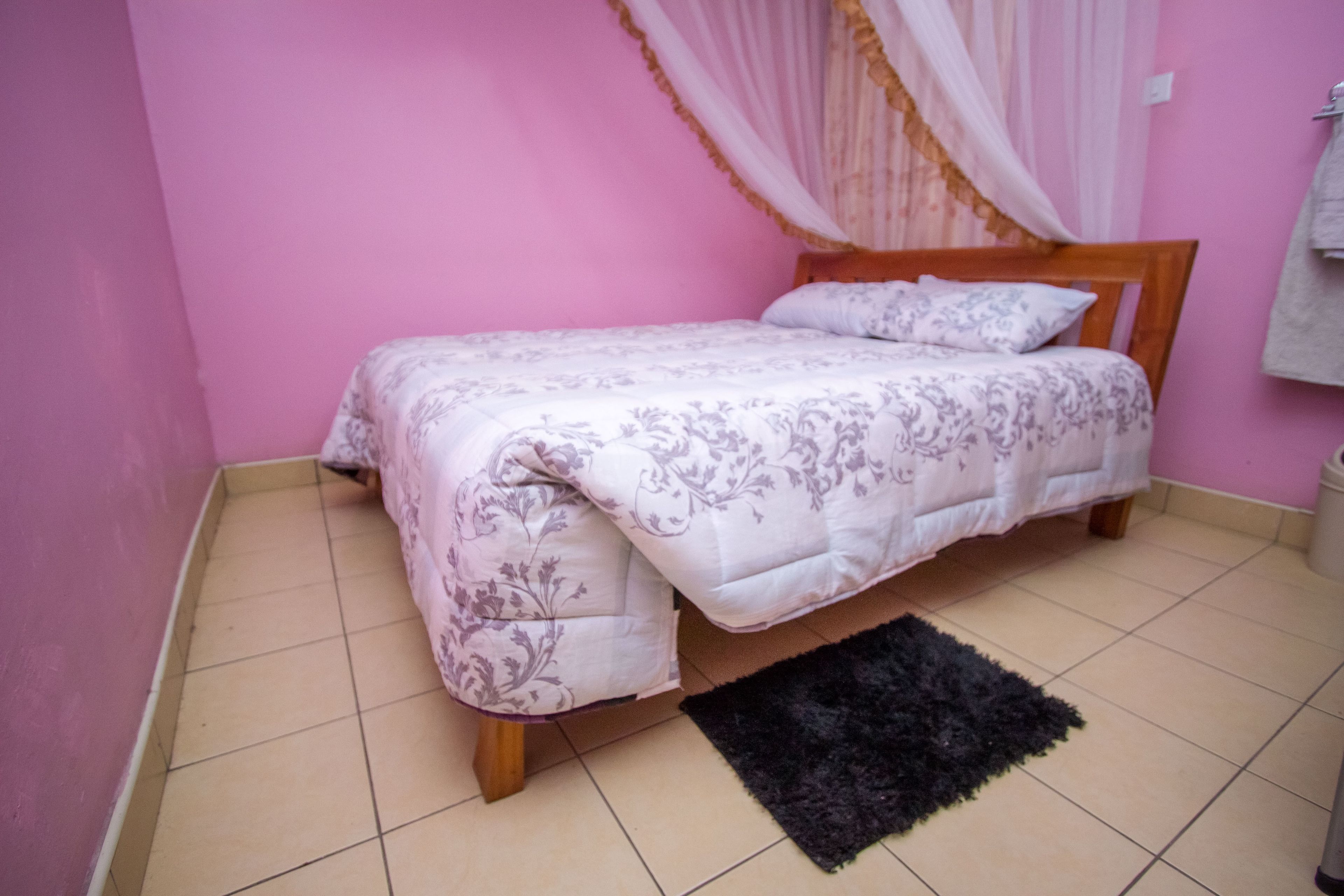 Une chambre à coucher avec un lit, un tapis noir et un mur rose.