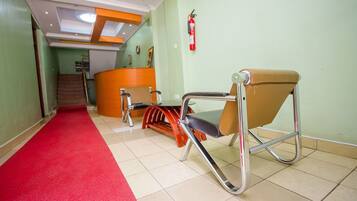 Un couloir avec un tapis rouge, un comptoir d’accueil, un extincteur et une chaise.