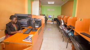 A reception area with a receptionist at a desk, multiple computer stations, and numbered seating areas. - Shamz Hotel Isiolo (Isiolo)