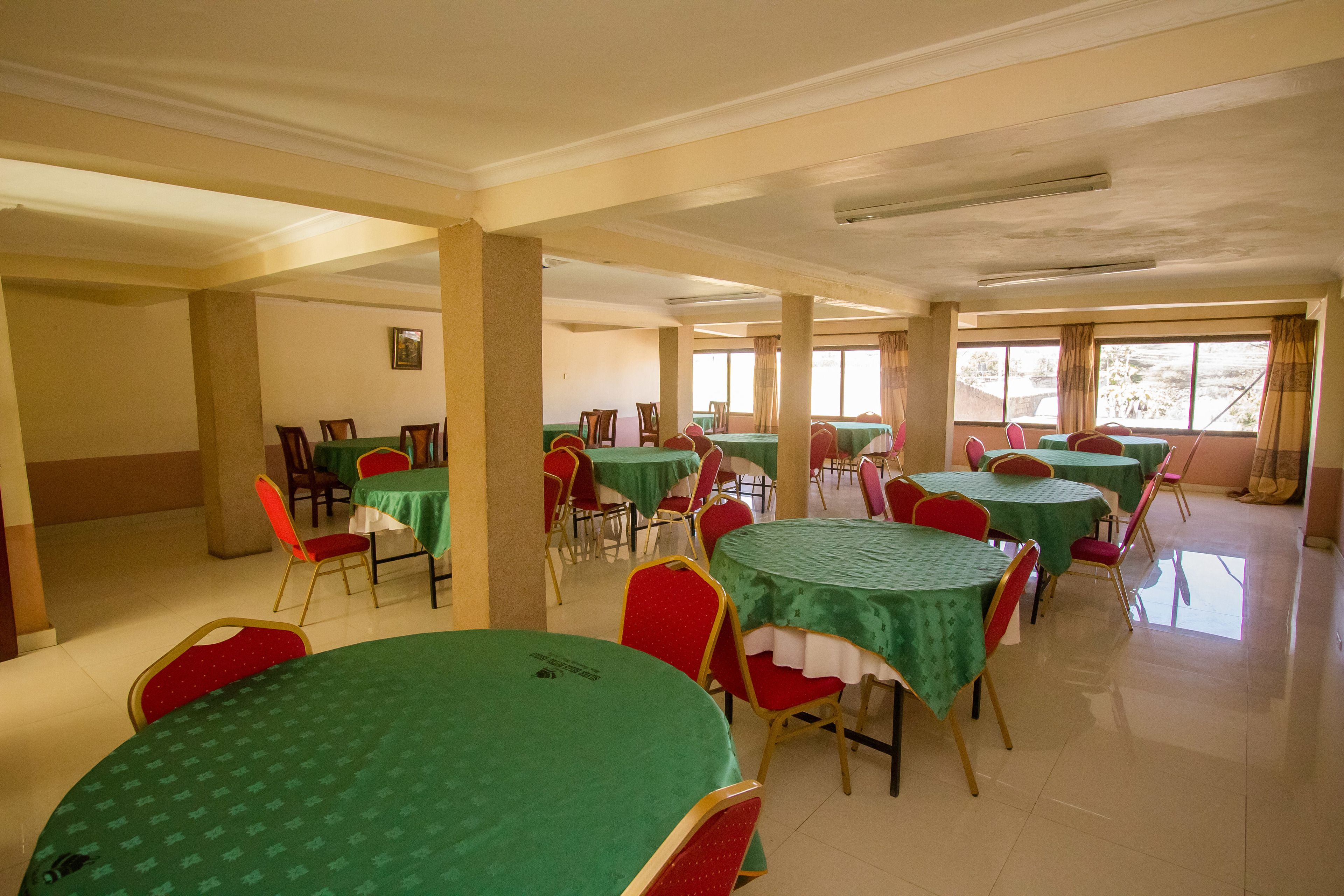 A dining area with round tables covered in green tablecloths, red chairs, and beige pillars.