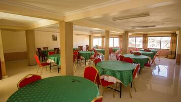 A dining area with round tables covered in green tablecloths, red chairs, and beige pillars.