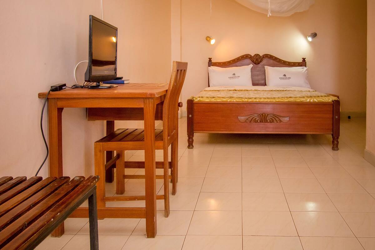 A bedroom with a wooden bed, a desk with a computer, a chair, and a bench.