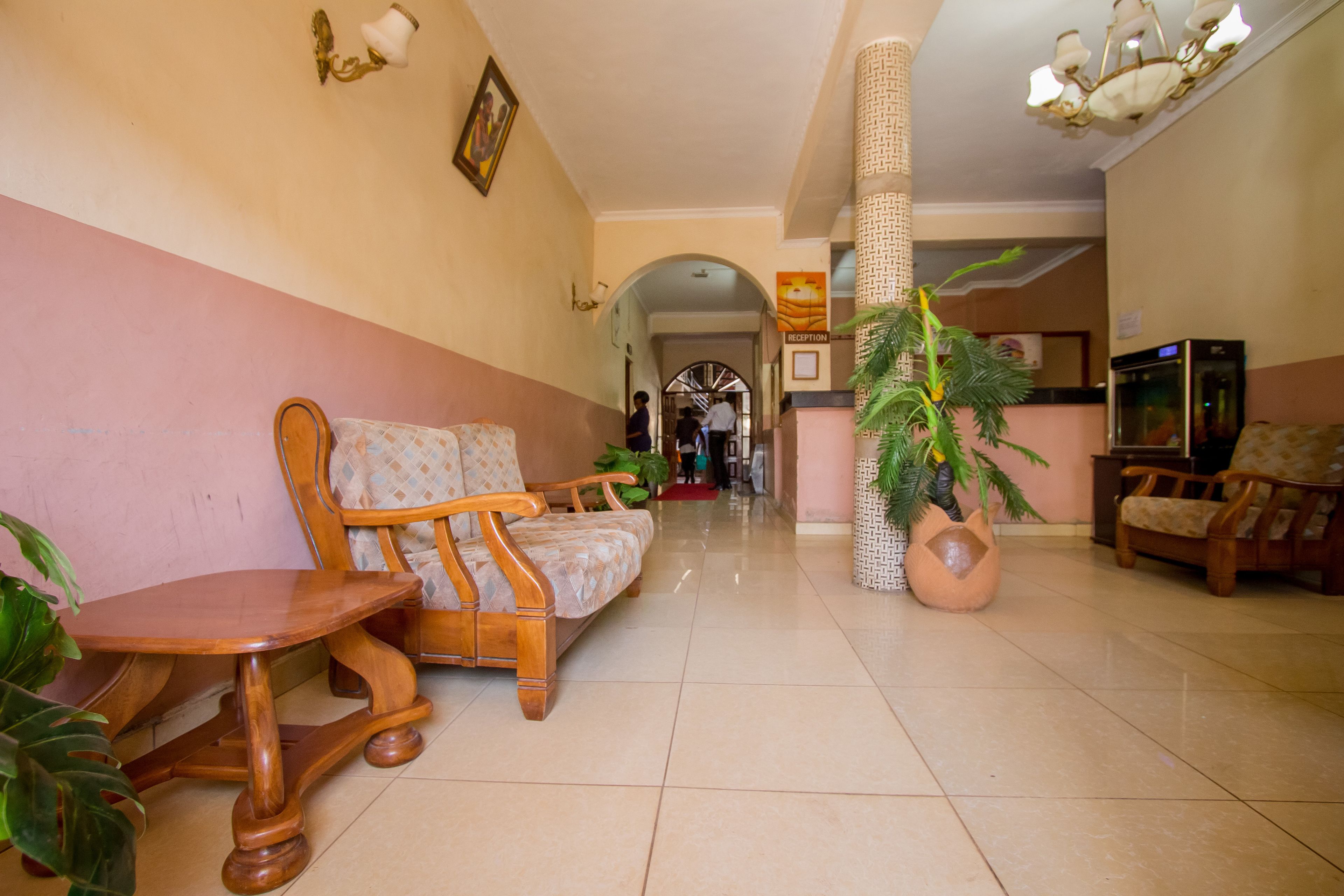 A reception area with a reception desk, a sofa, a wooden chair, a potted plant, and a refrigerator.