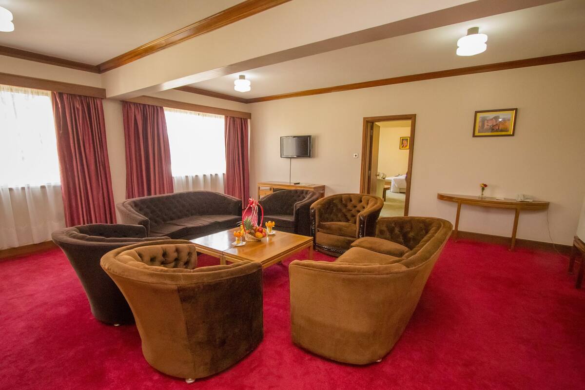 A room with a red carpet, a television mounted on the wall, and a wooden table with a vase of flowers.