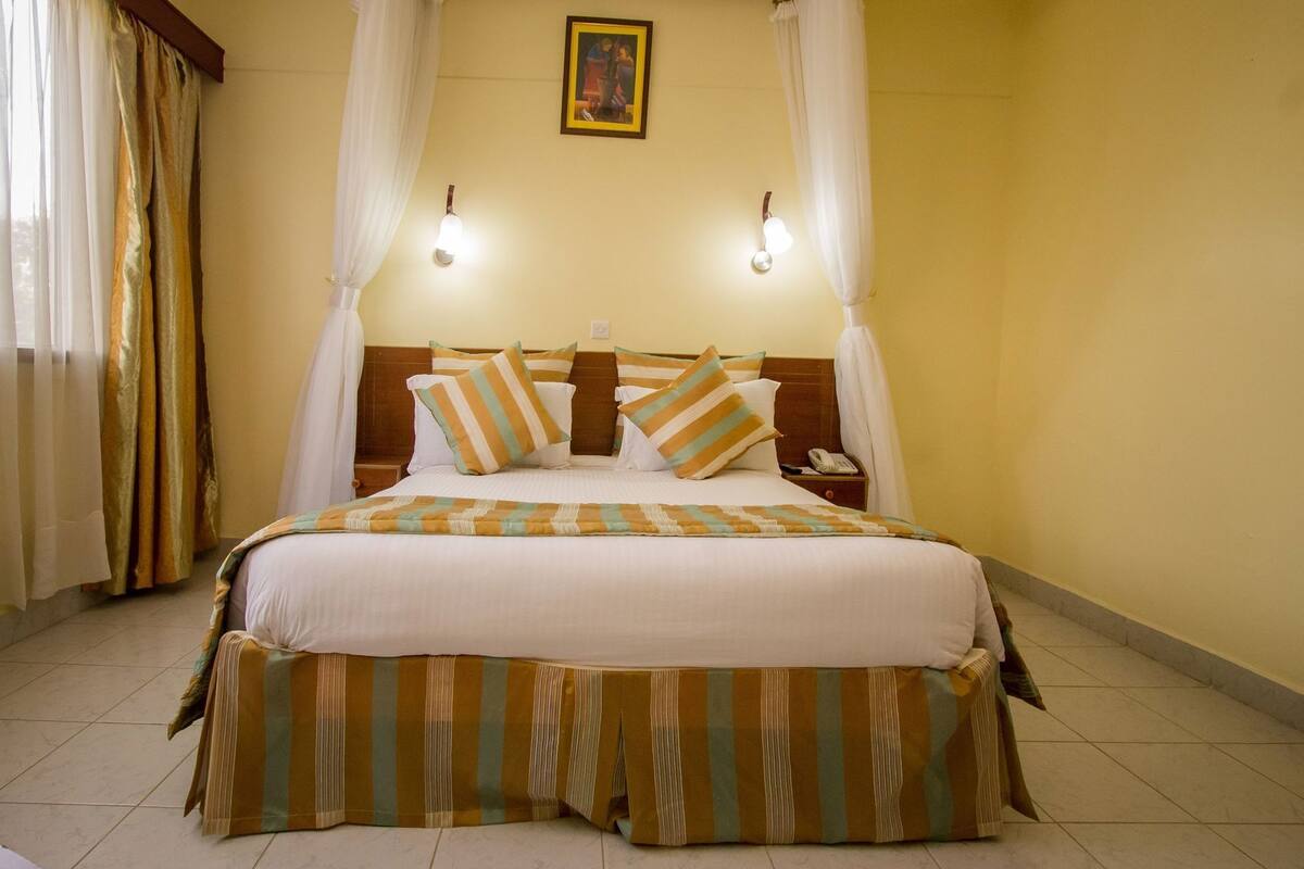 A bed with striped bedding, a nightstand with a phone, and a wall-mounted light fixture.