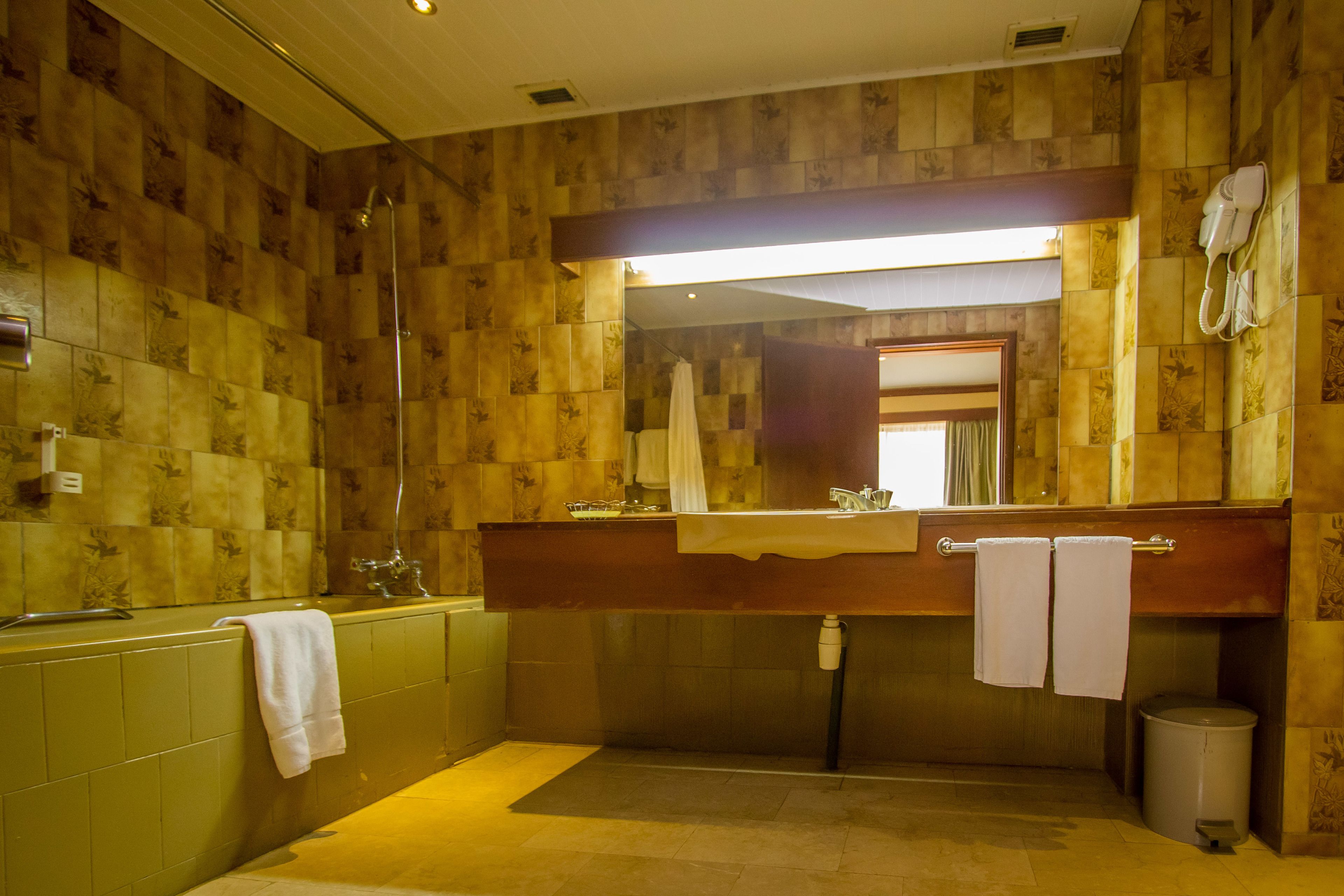 A bathroom with a wooden wall design, a large mirror, a sink with a towel rack, and a handheld showerhead.