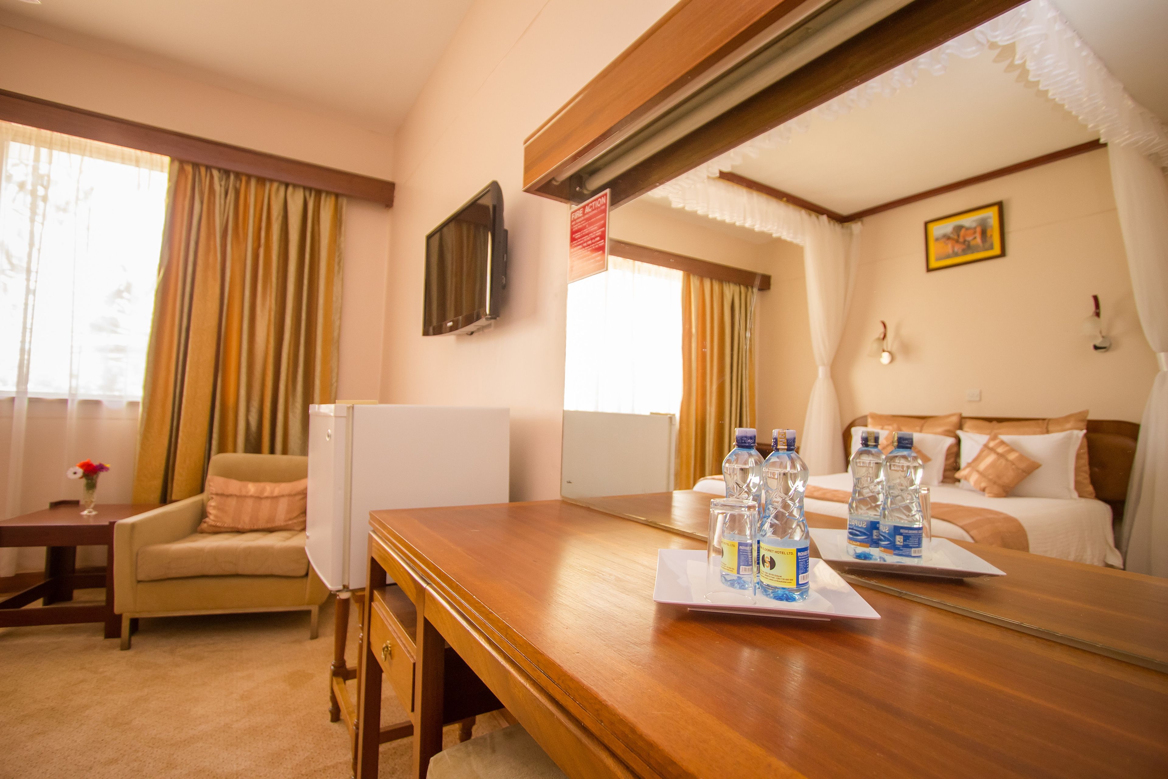A hotel room with a wooden desk, a chair, a bed with pillows, a TV mounted on the wall, and a window with curtains.