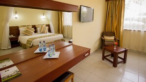 Habitación de hotel con cama, mesita de noche con botellas de agua, escritorio, silla, televisor y cortinas.
