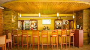 Zona de bar con sillas de madera y una barra, con pared de piedra y techo de madera.