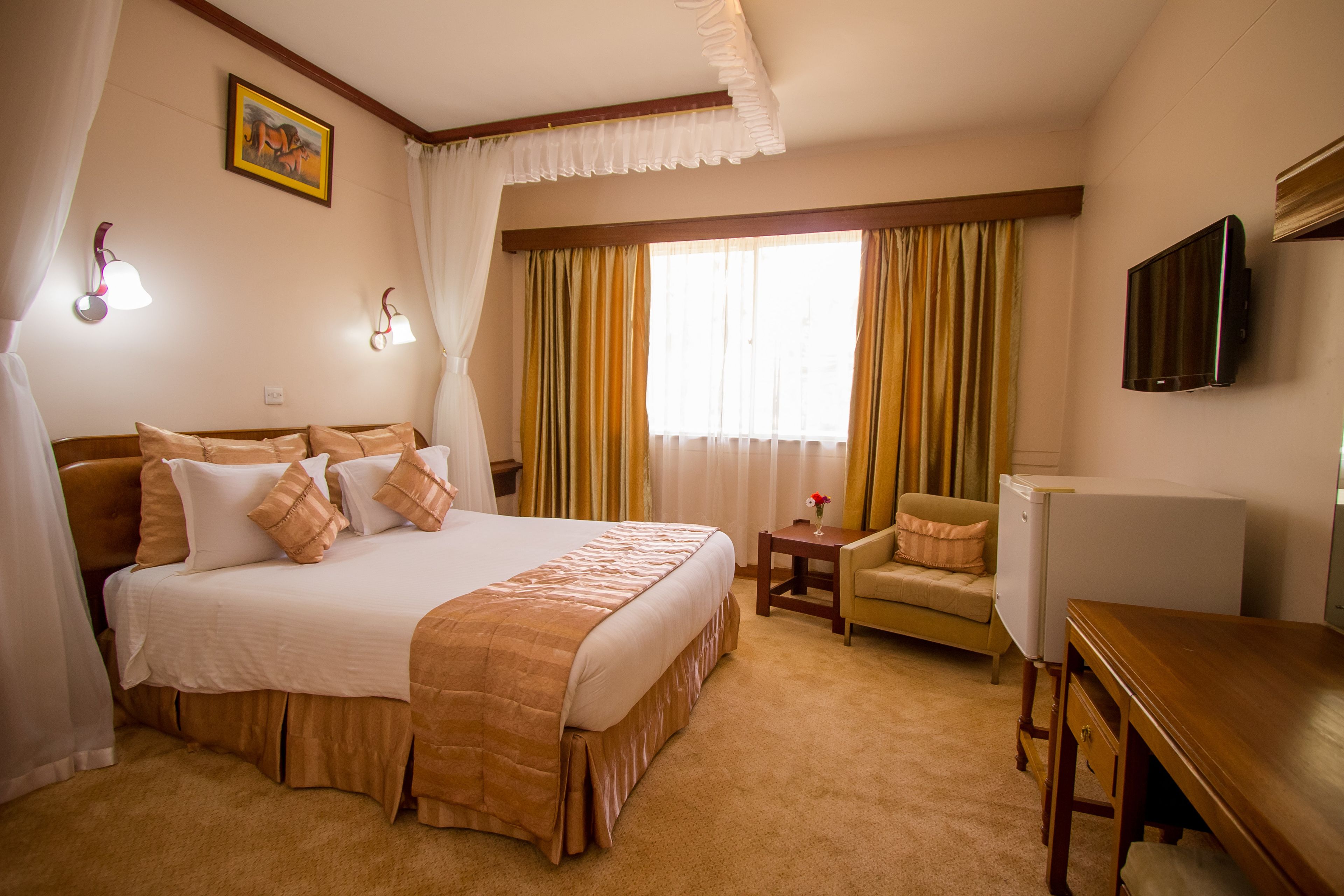 Ein Hotelzimmer mit einem großen Bett, einem Sessel, einem Schreibtisch, einem Fernseher und Vorhängen.