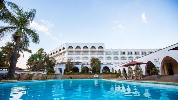 Un hotel con piscina, palmeras y un edificio blanco con ventanas arqueadas.
