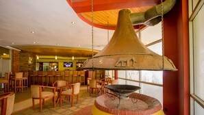Un restaurante con un horno de ladrillo central, sillas de madera y una barra al fondo.