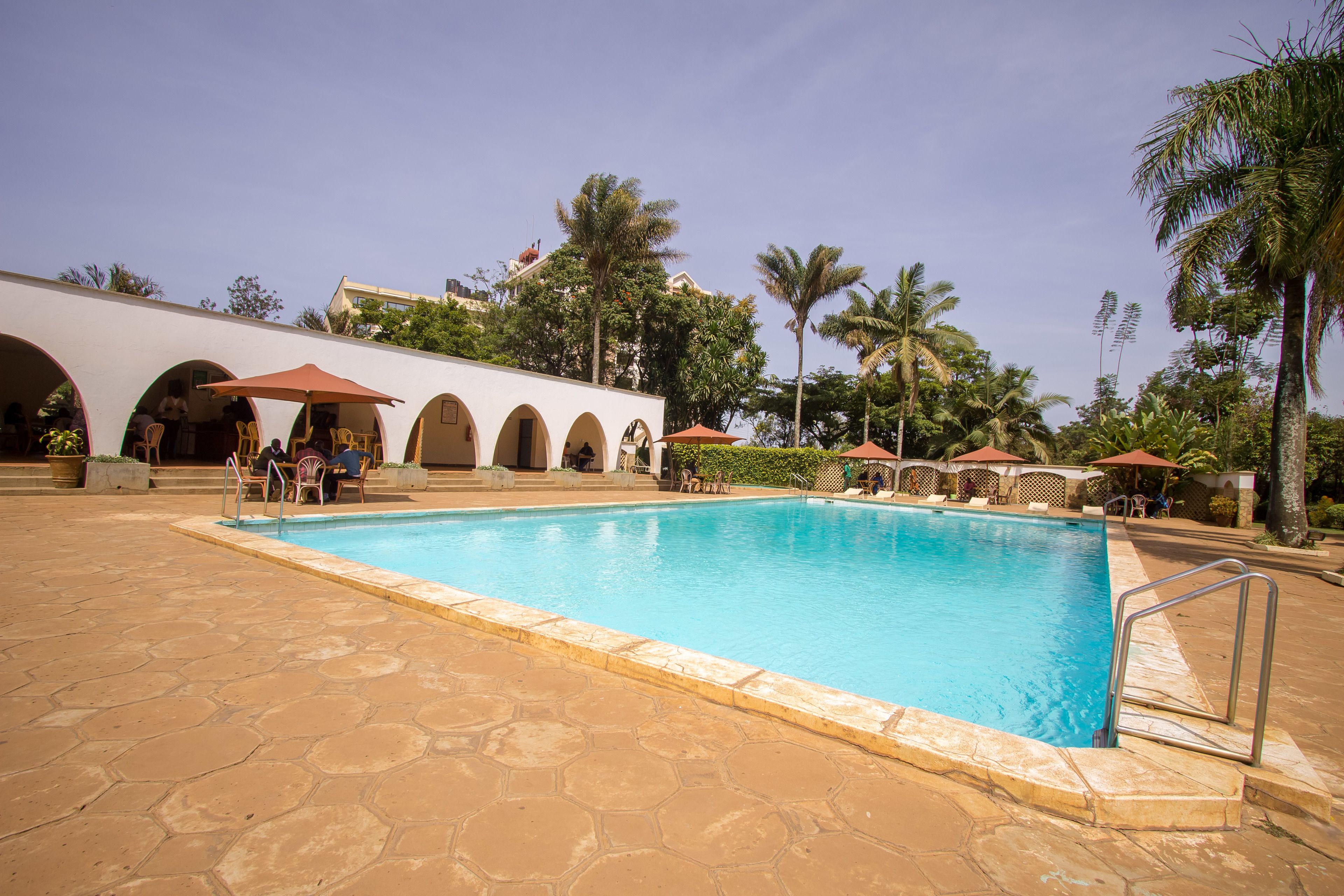 A swimming pool with a tiled deck, surrounded by palm trees and covered seating areas.