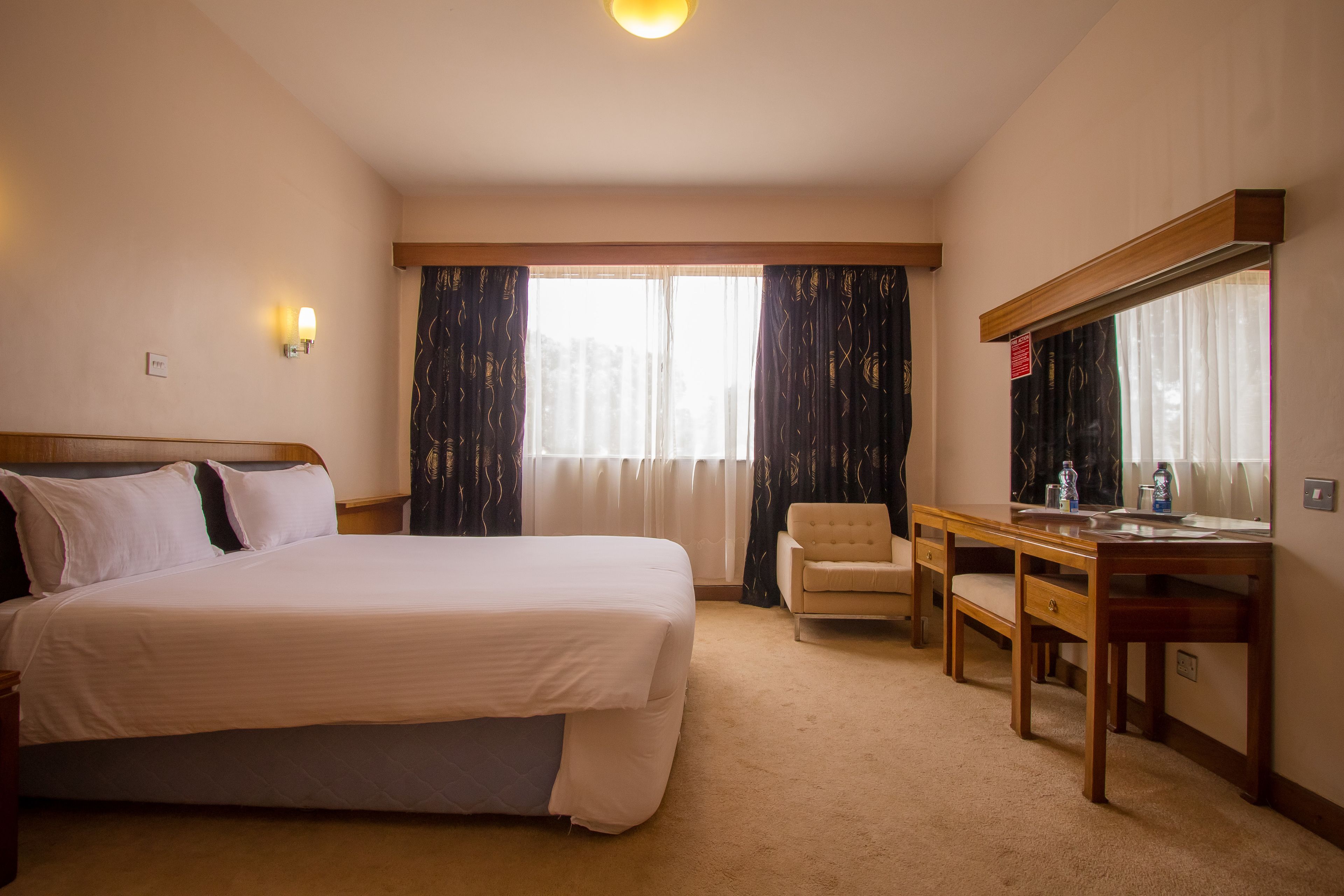 A hotel room with a bed, a desk, a chair, and a large mirror.