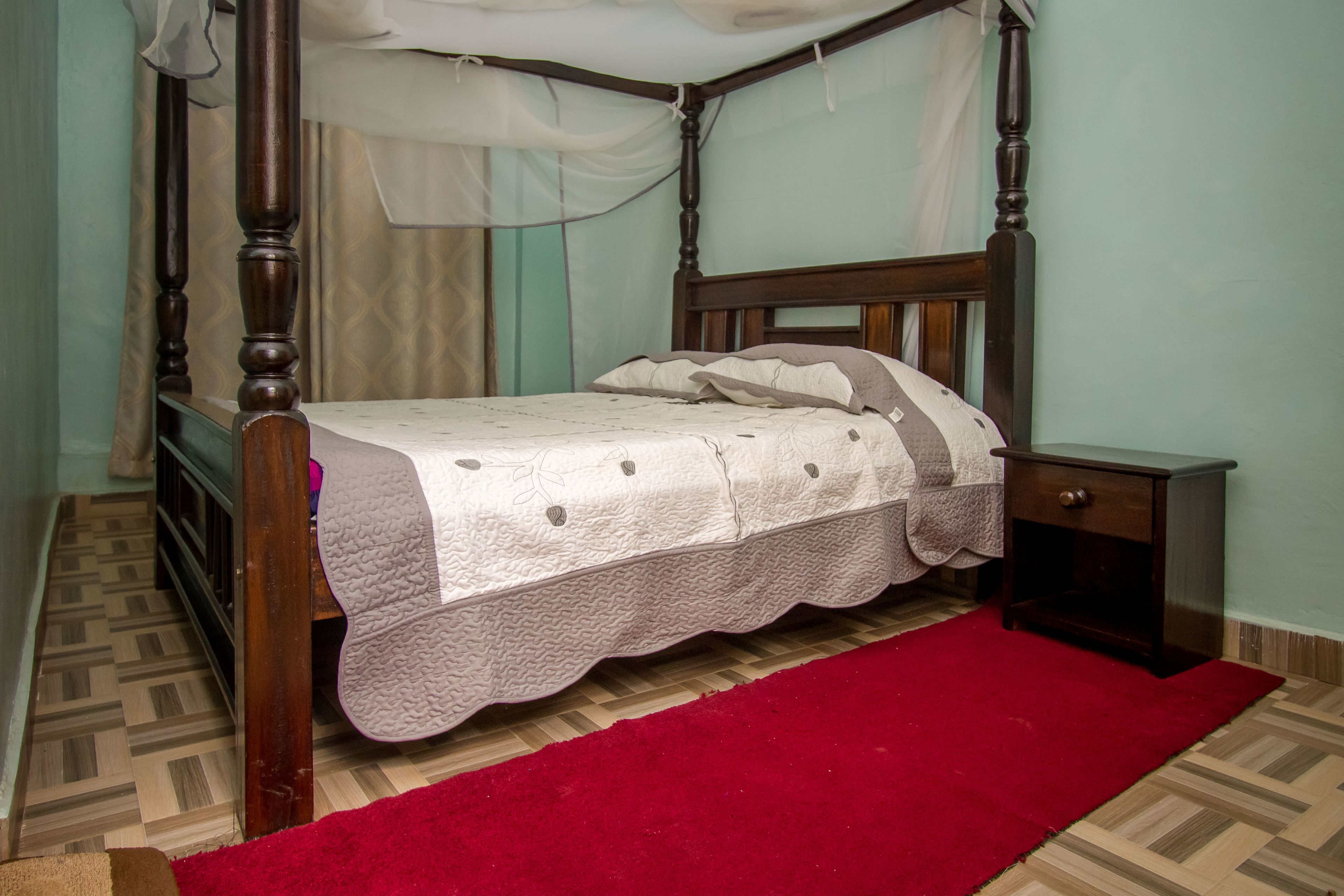 A four-poster bed with a white bedspread and a red runner.