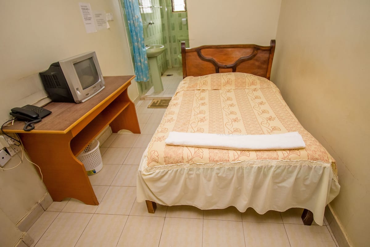 A small, neatly arranged bedroom with a single bed, a wooden desk with a television, and a telephone.