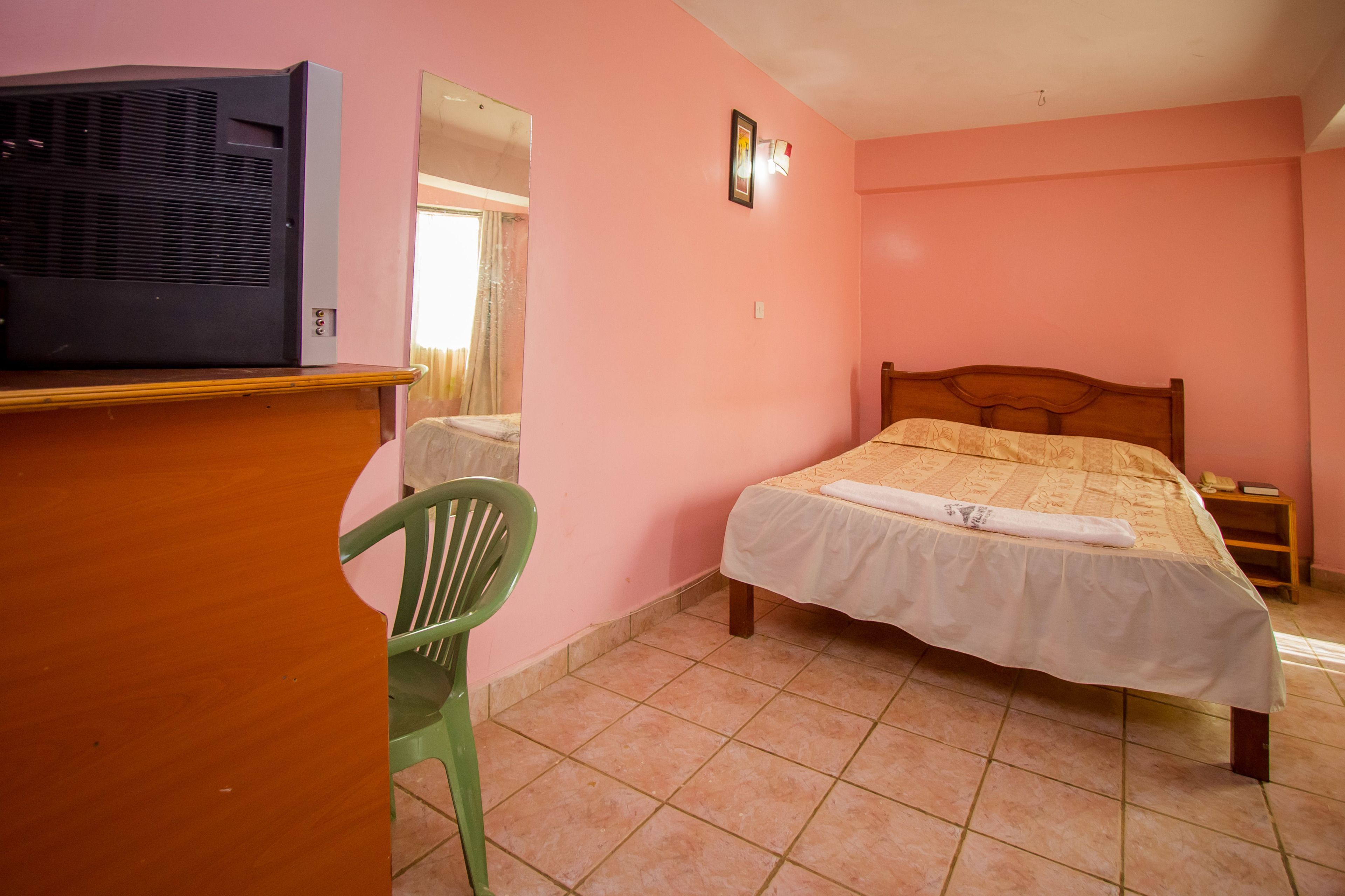 Ein Schlafzimmer mit einem Bett, einem Schreibtisch mit Fernseher, einem Sessel und einem Spiegel.