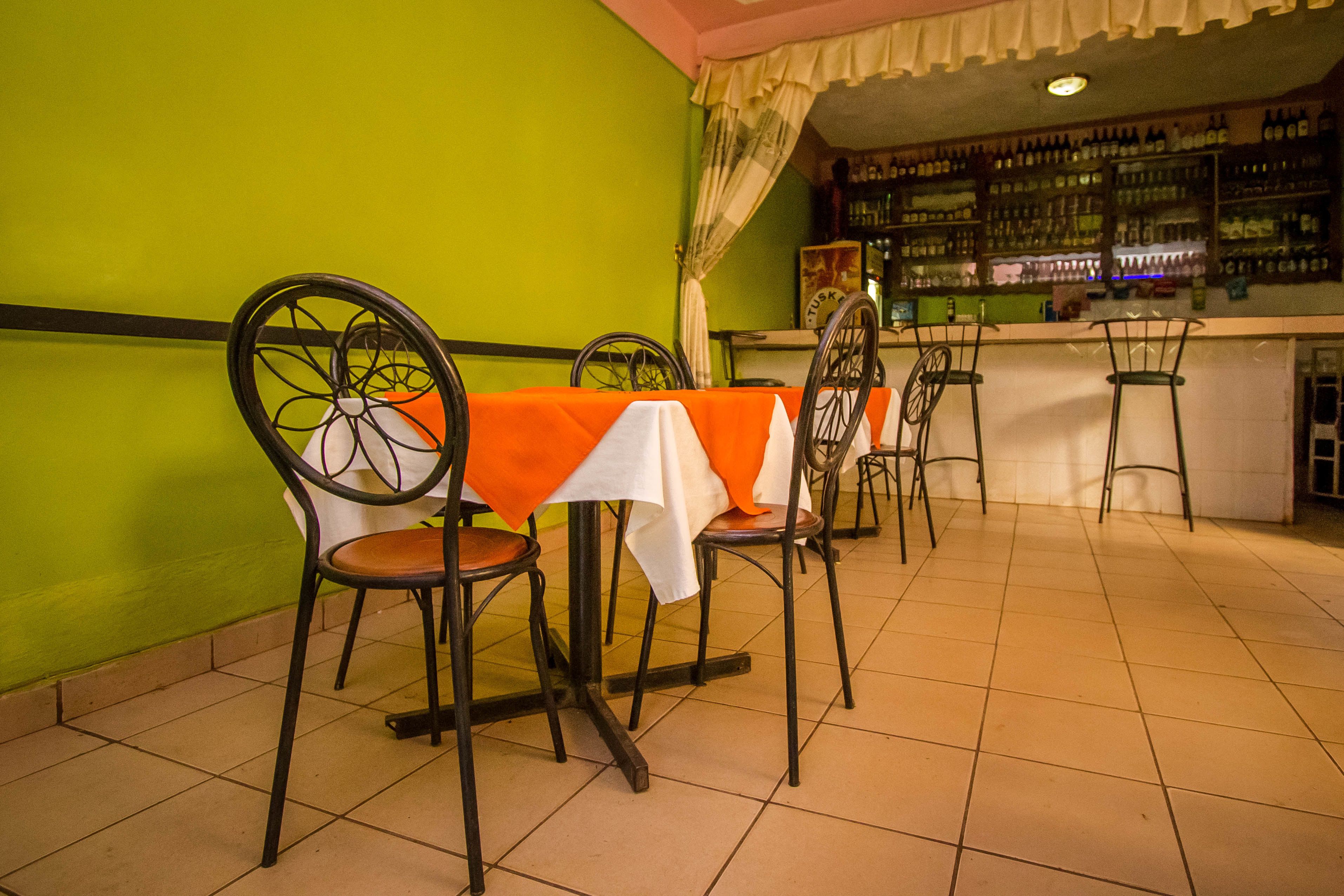 A restaurant with a green wall, a bar area with shelves of bottles, and a table with a white and orange tablecloth.