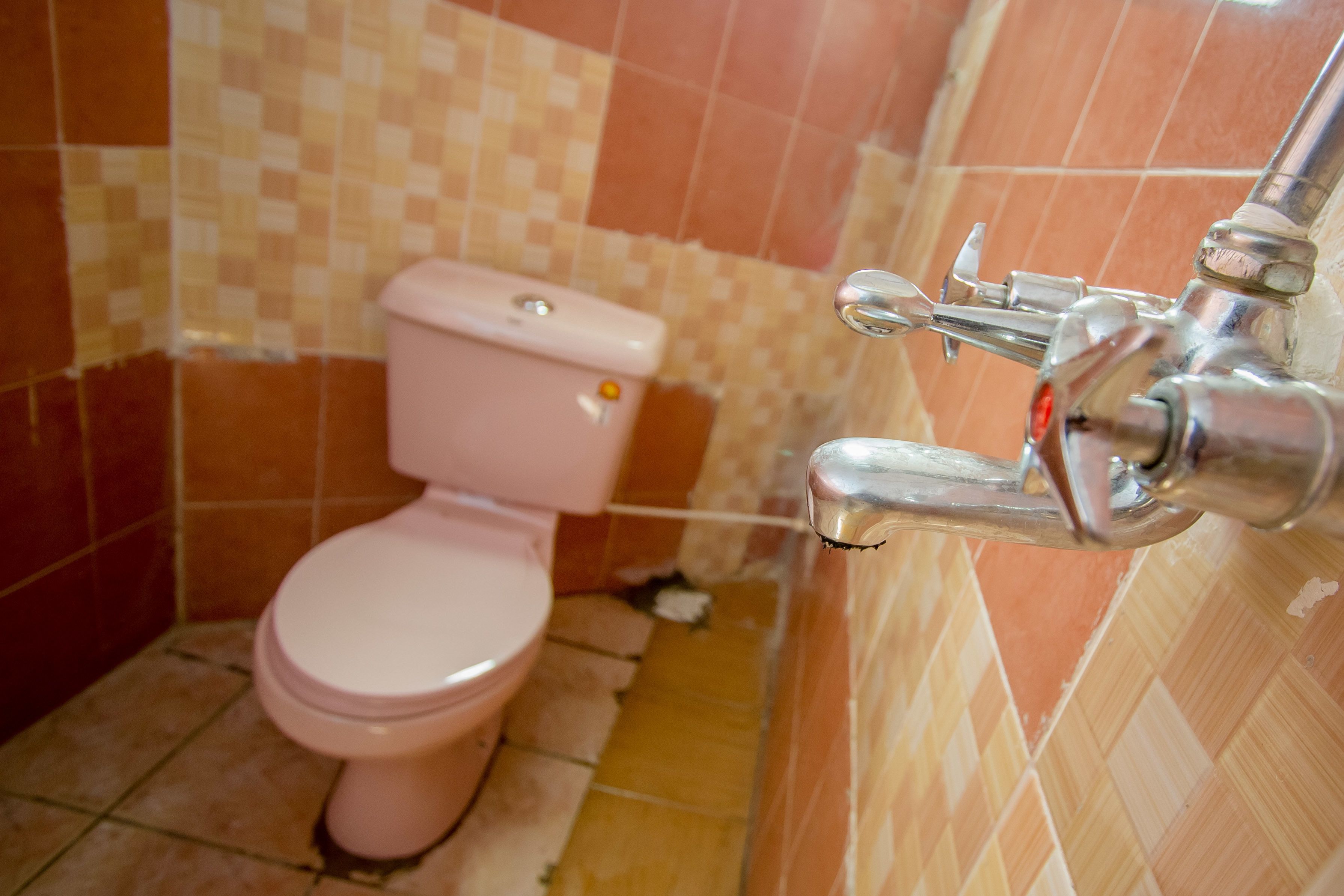 A bathroom with a pink toilet, a tiled wall, and a chrome faucet.
