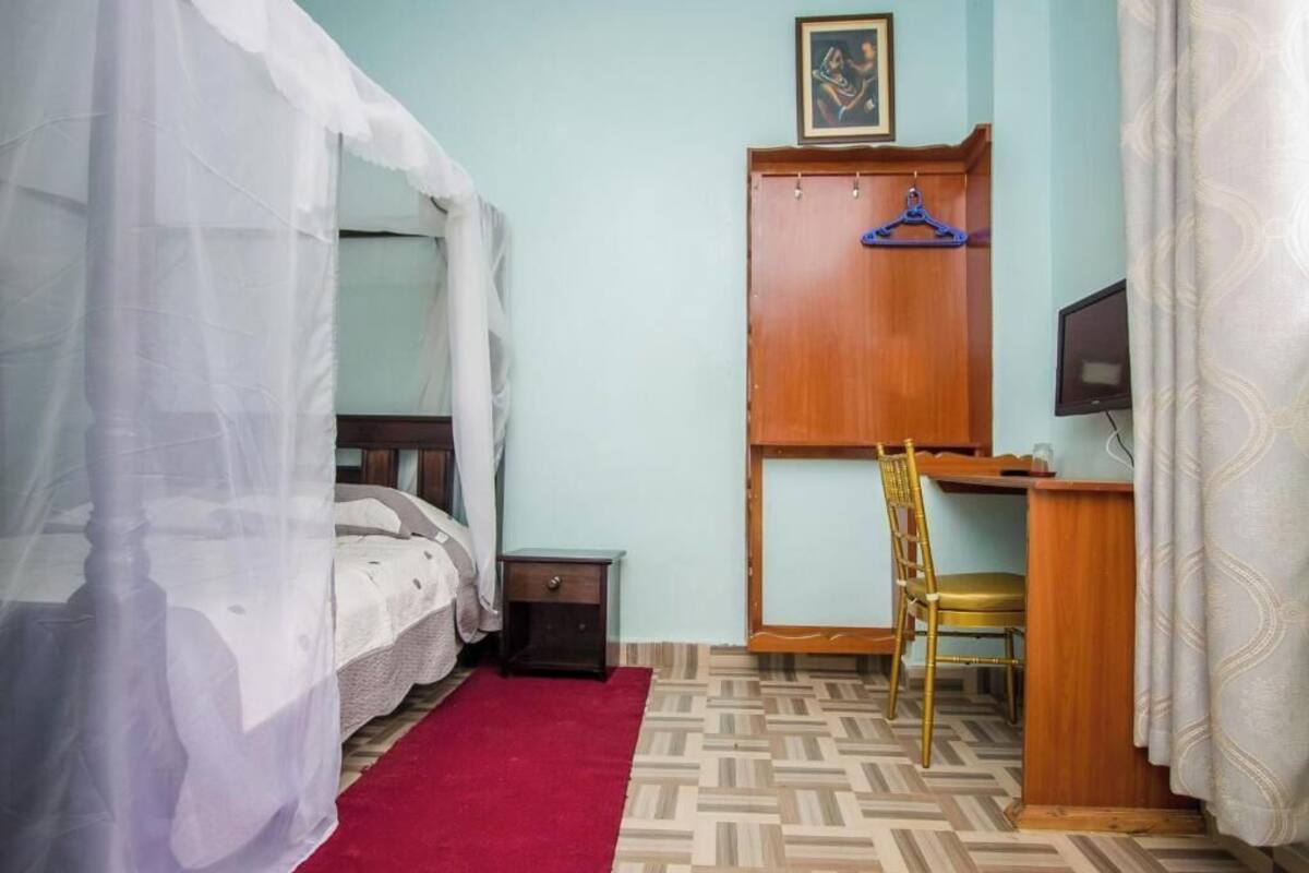 A bedroom with a bed under a canopy, a desk with a chair, a television, and a wardrobe.