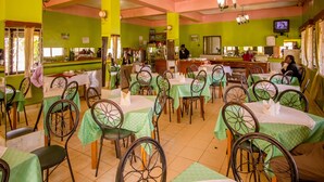 Un restaurante con paredes verdes y mesas, una zona de bar y una pantalla de televisión.